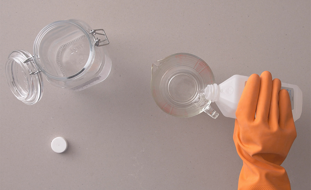A person wears rubber gloves to pour rubbing alcohol into a measuring cup.
