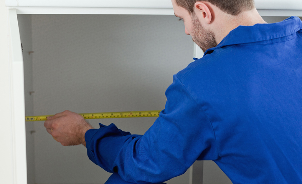  A man uses measuring tape to measure the width and depth of his sink base cabinet.
