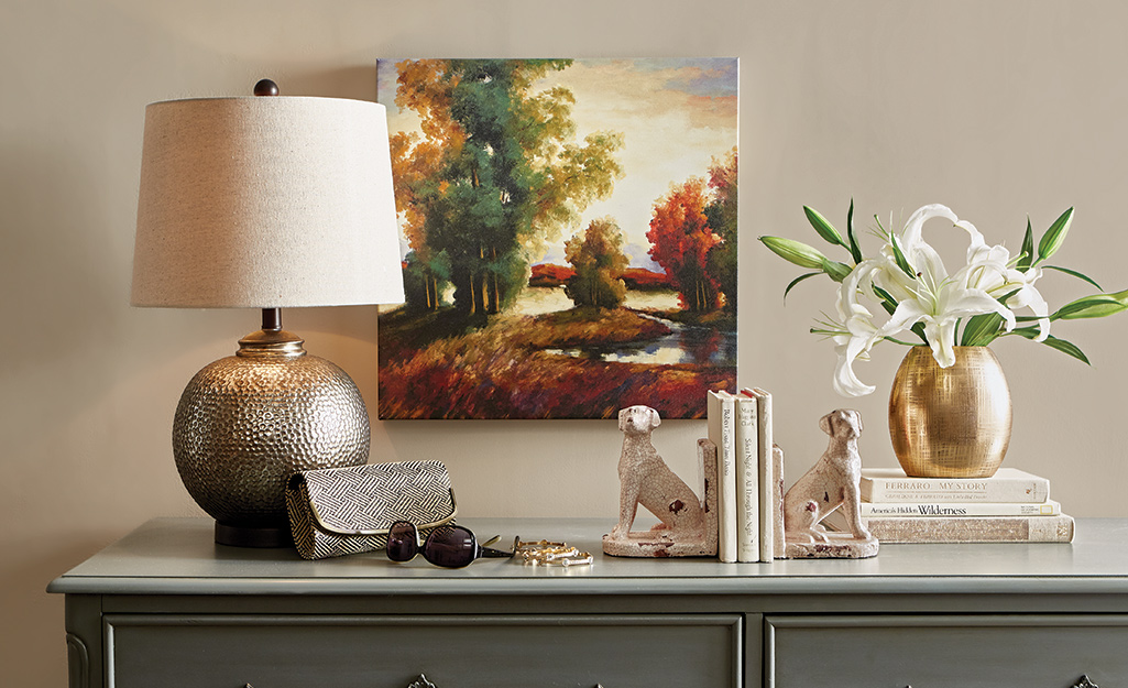 A metallic lamp with a simple barrel lamp shade sits next to other home decor on a side table.