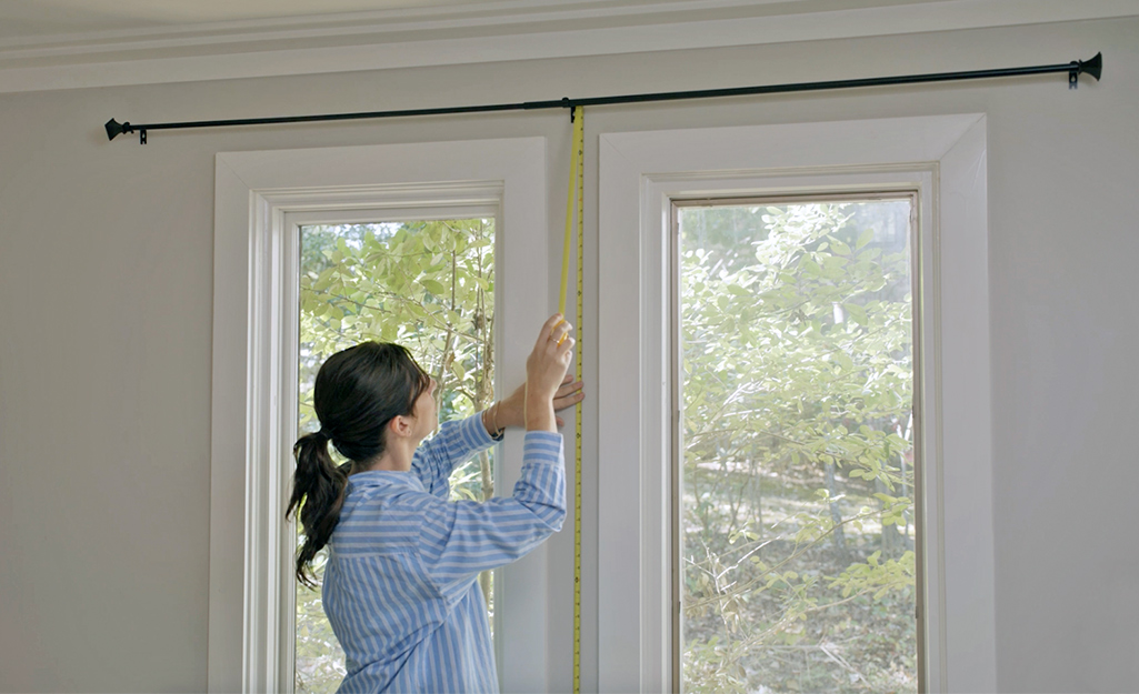 Someone measuring from the floor to the bottom of a curtain rod.