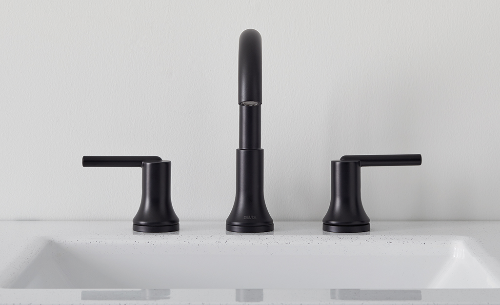A widespread black faucet and sink handles is mounted to a white bathroom countertop.