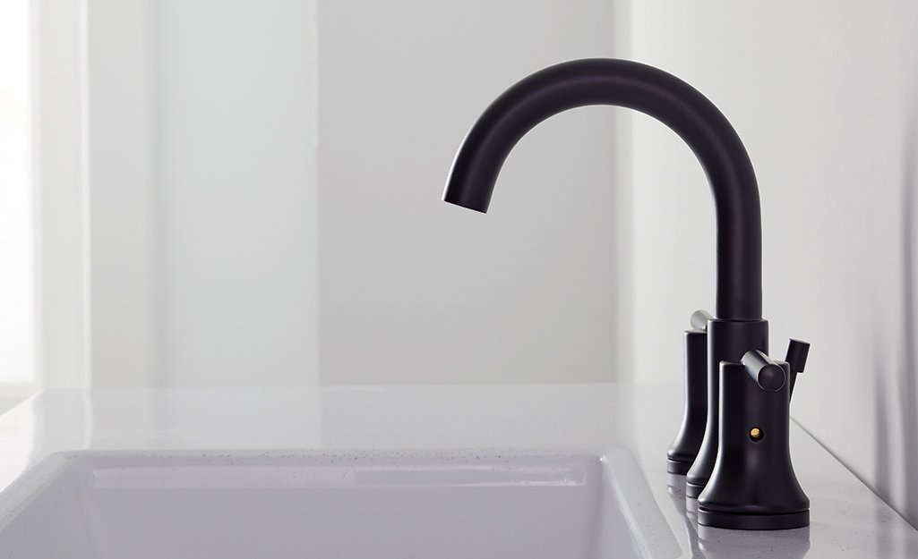 The spout of a black bathroom faucet reaches over the sink.