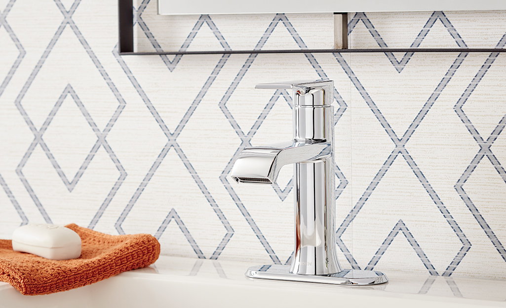 A single-hole faucet stands against bathroom wallpaper with a diamond pattern.