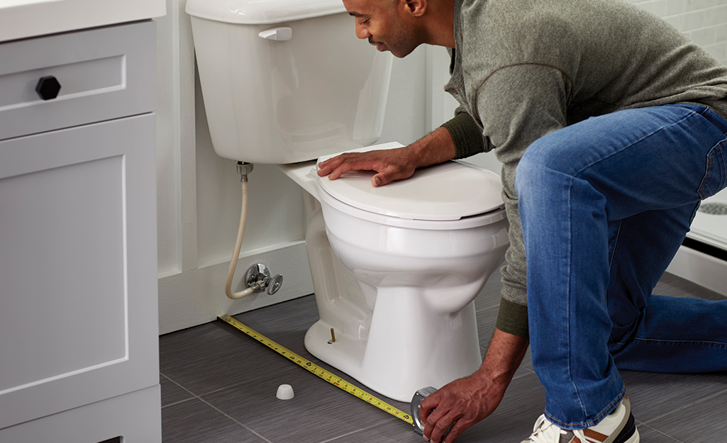 Person using a tape measure to measure the base of a toilet