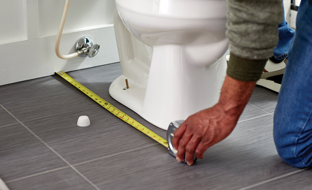 Person measuring a toilet base with a tape measure