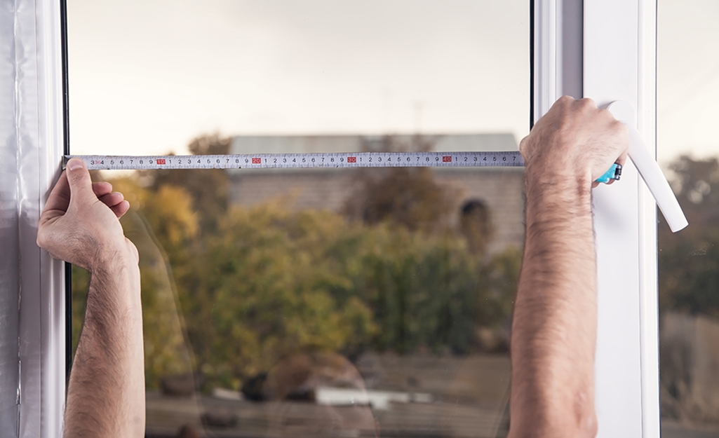 A person measures a window width using a tape measure.