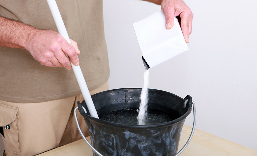 A man pours grout powder into a bucket.