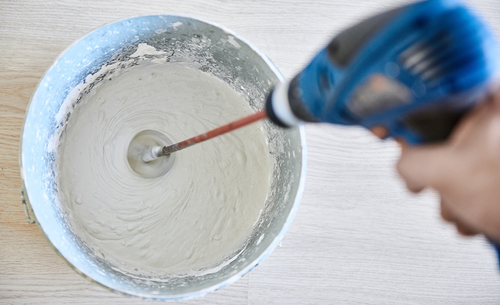 Drill with a grout mixing attachment mixes grout in a bucket.