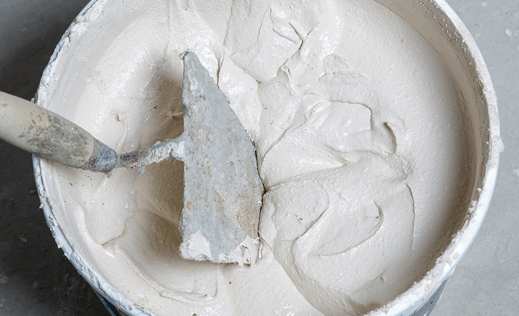 A trowel in a bucket of mixed grout.