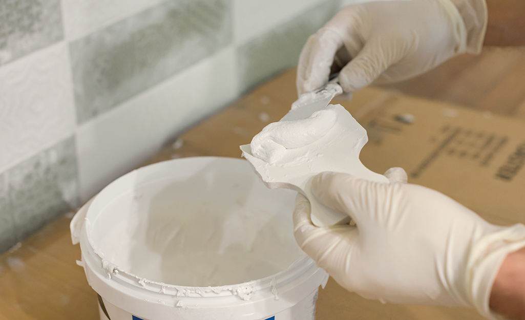 A person scoops epoxy grout from a bucket.