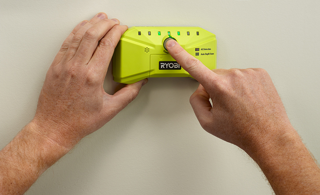Person holding a stud finder against a wall.