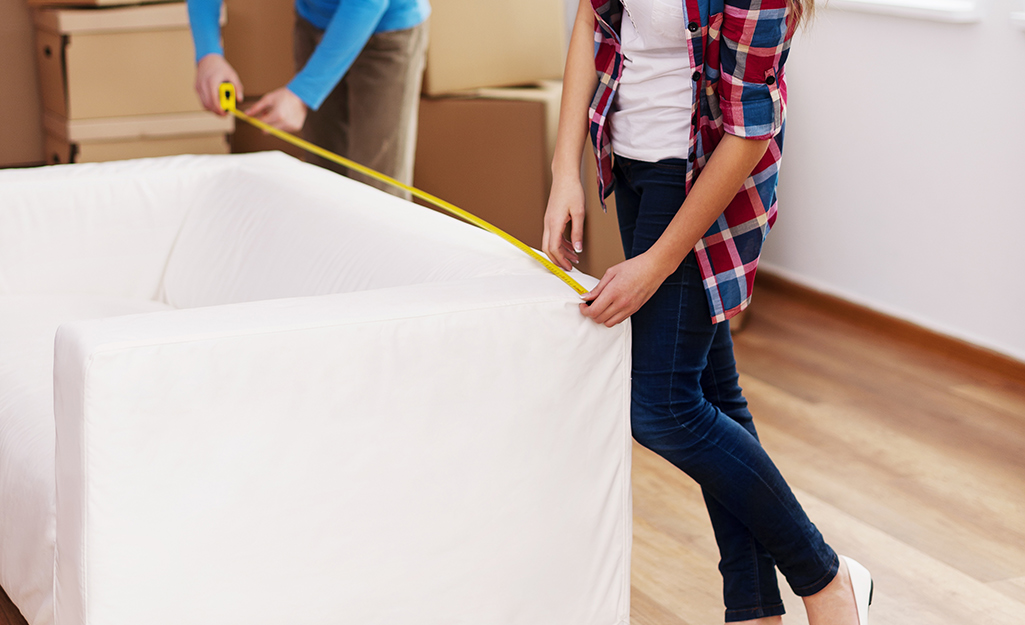 Two people measure the back of a couch.