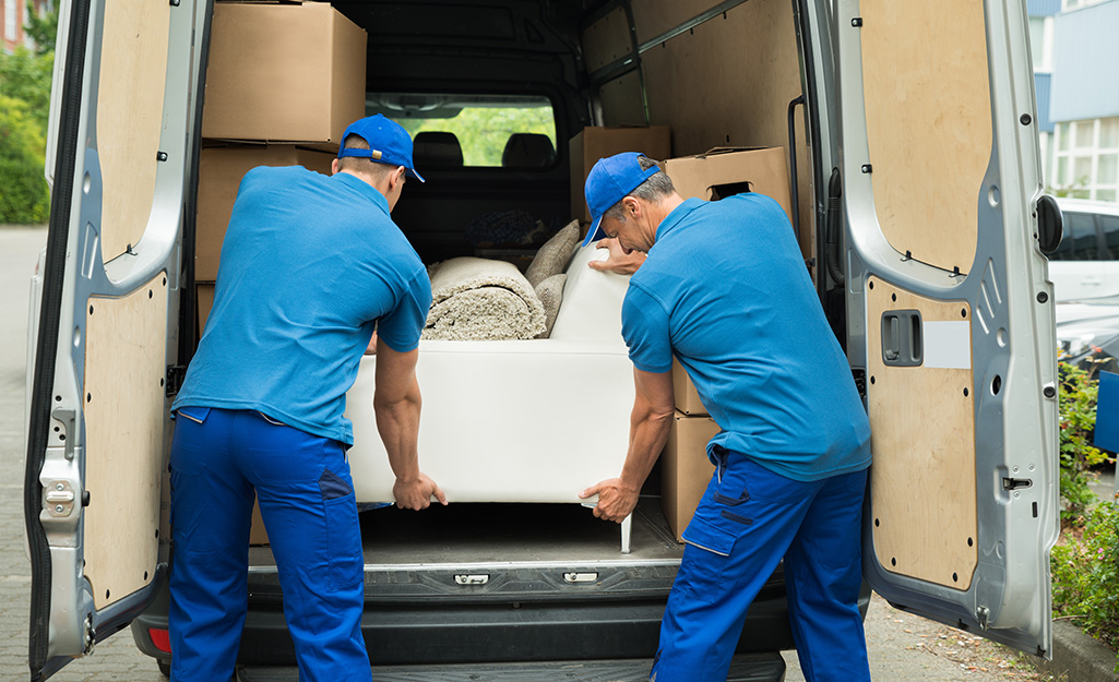 Two movers put a couch into the back of a moving van.