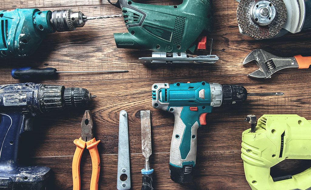 Drills, pliers and wrenches laid out on a wood table.