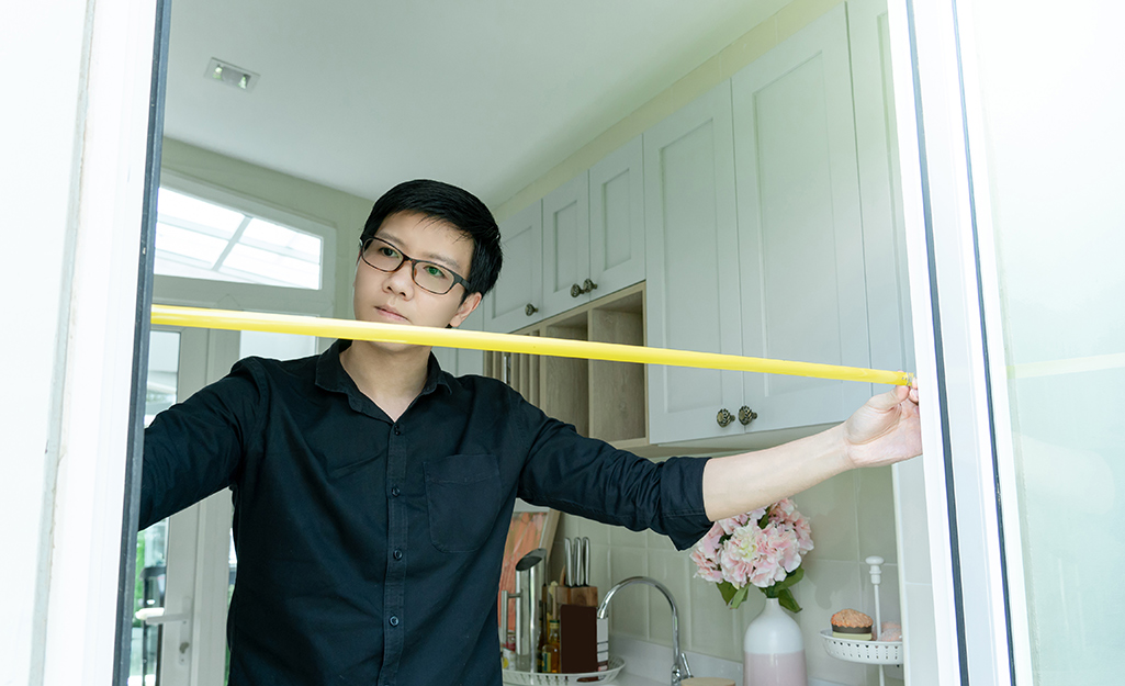 Man measuring a doorway with a yellow measuring tape.