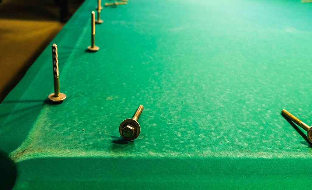 A pool table with unscrewed bolts placed on its felt.