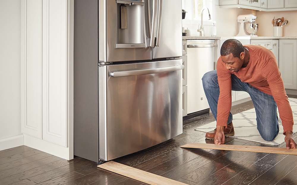 A person laying vinyl planks to protect floors while moving a refrigerator.