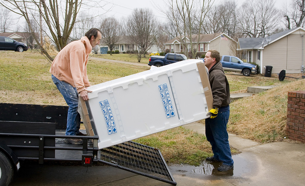 Two people loading a refrigerator onto a truck.