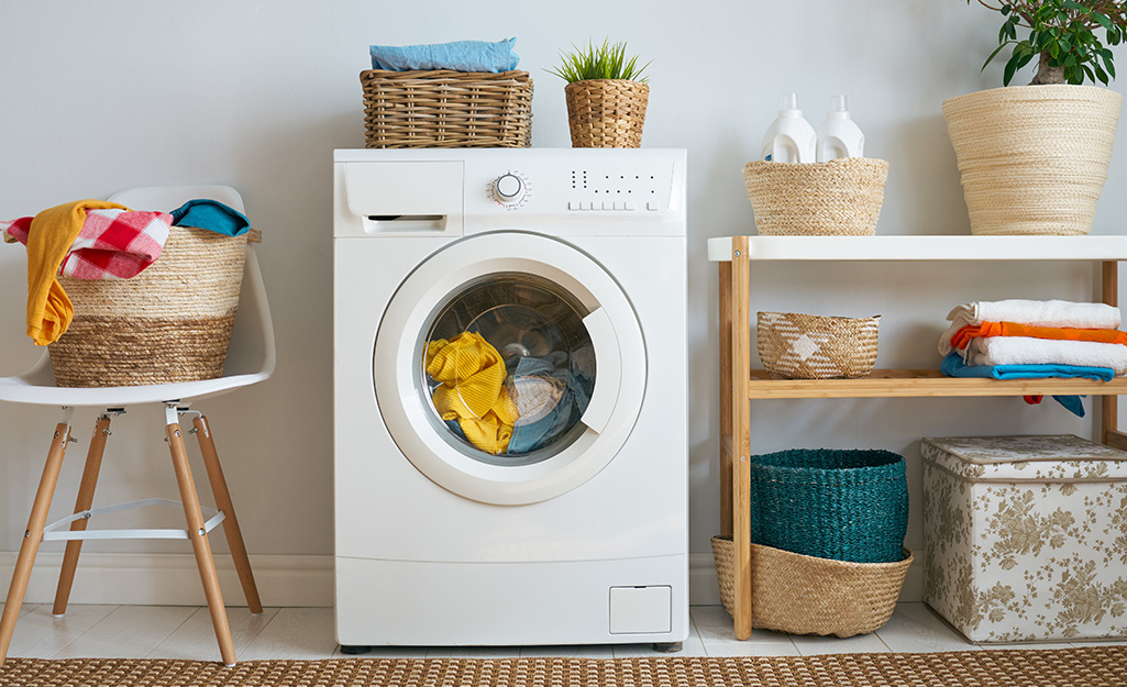 A washer sitting against a wall surrounded by baskets of clothes.