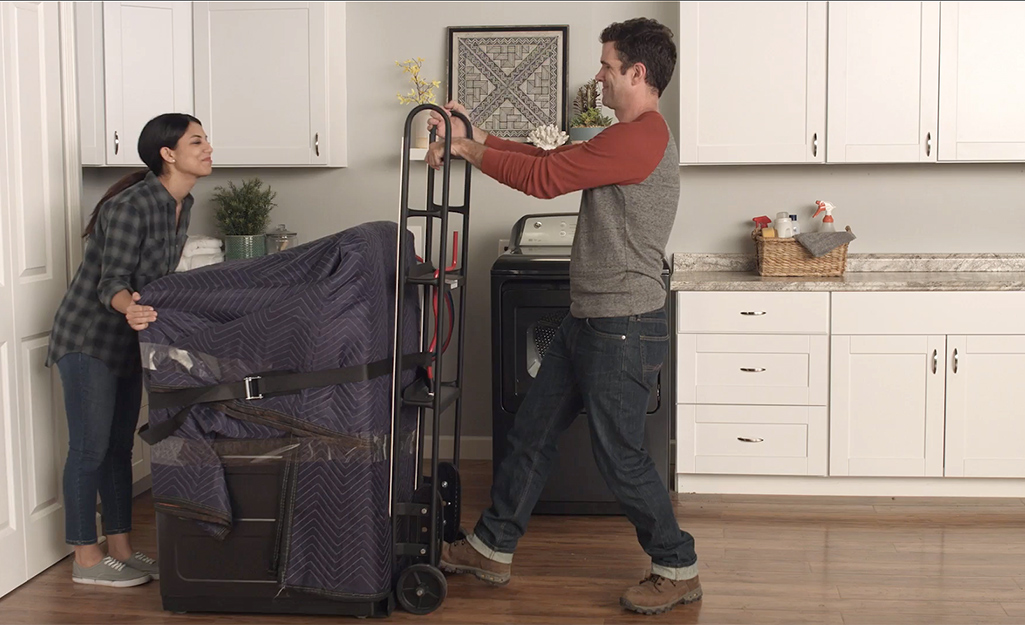 Couple placing wrapped washing machine onto a hand truck.