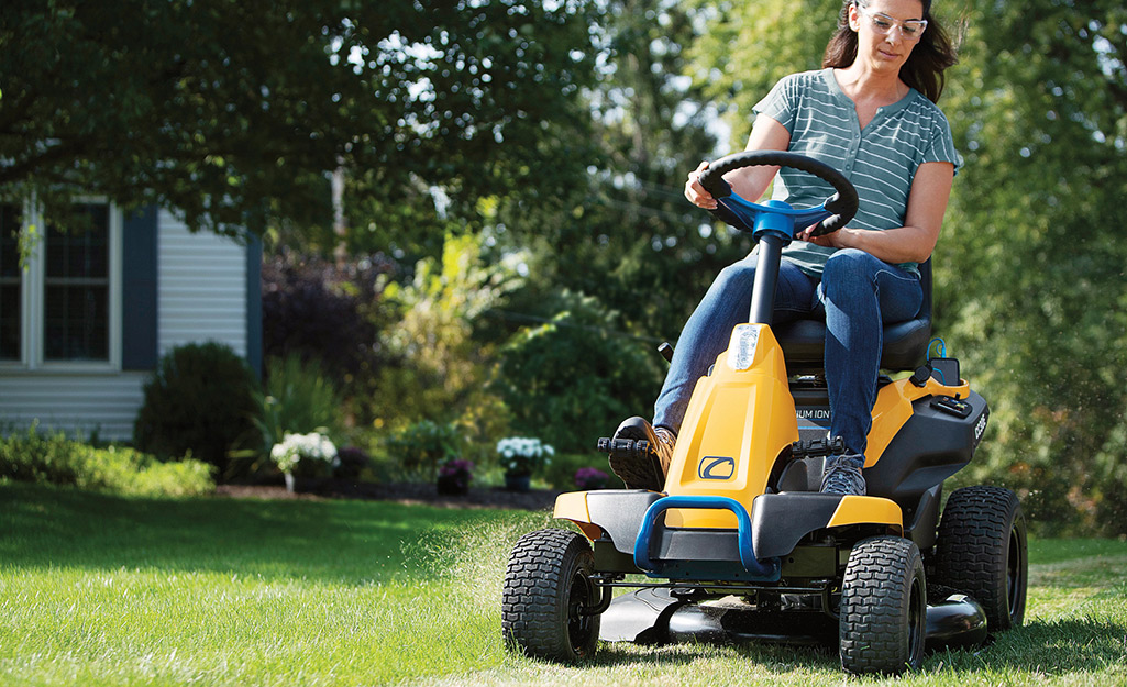 A woman cuts grass with a riding lawn mower.