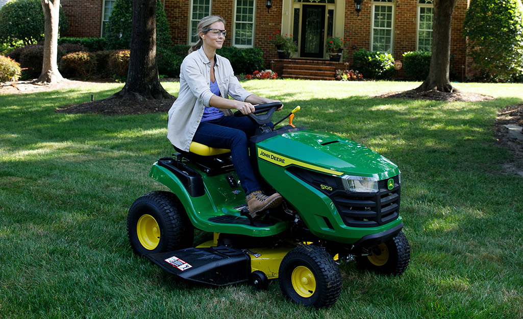 A woman mows a lawn with a lawn tractor.