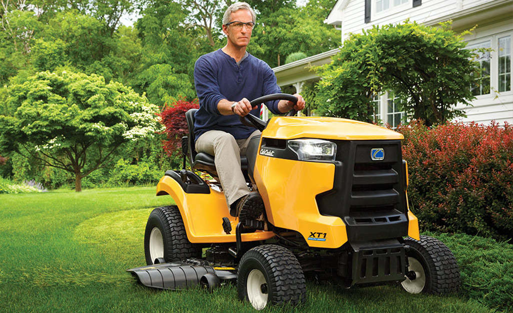 A man uses a garden tractor to mow a lawn.