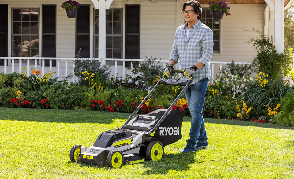 A man uses a push mower to mow a lawn.