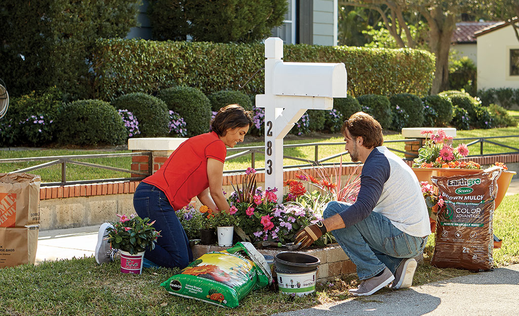 Two people planting flowers and laying mulch around a mailbox.