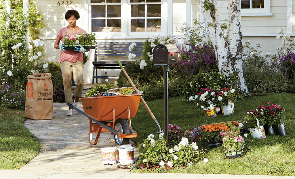 A person carrying flowers to plant in a mulched garden bed.