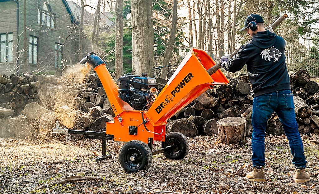 A person feeds branches into a chipper shredder.