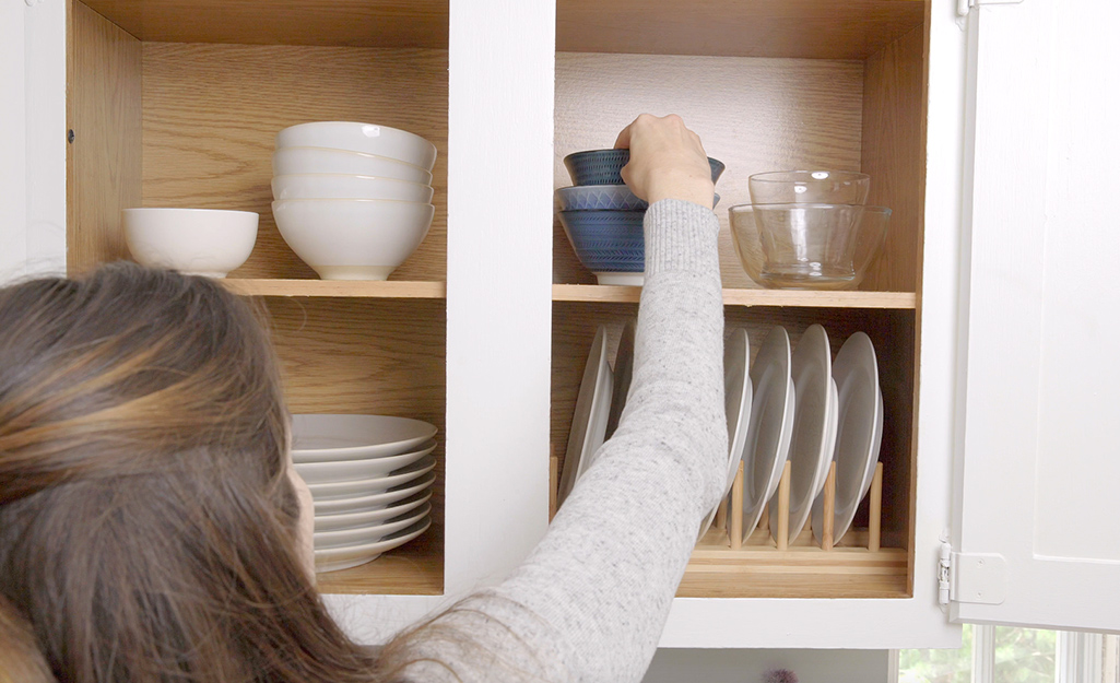 A person sorts and stacks plates to organize them in a cabinet.