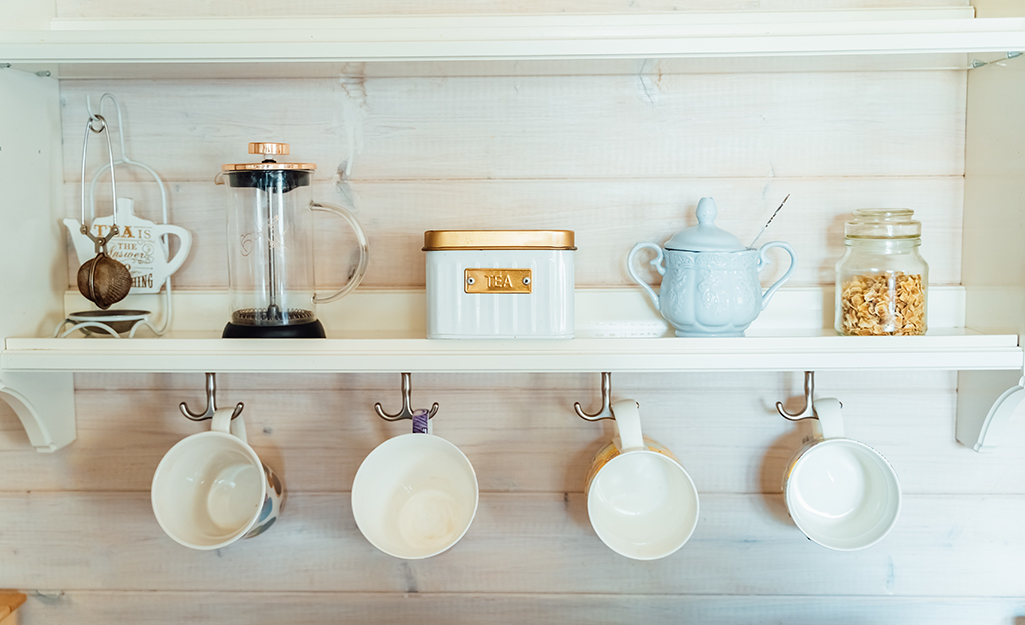 Coffee mugs hang from hooks under a cabinet shelf.