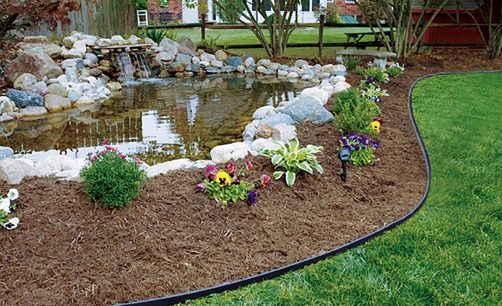 A long run of flexible strip edging runs along a garden border by a water feature.