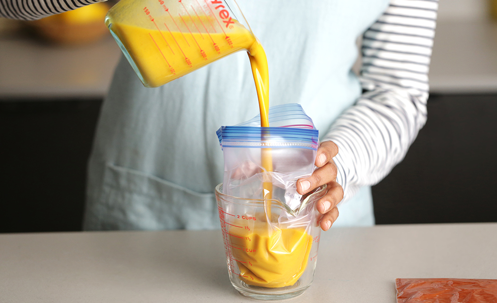 A woman pours soup into a freezer bag. 