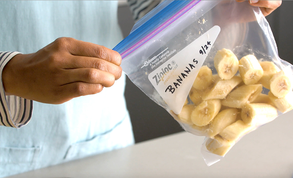 A woman seals a freezer bag filled with sliced bananas.
