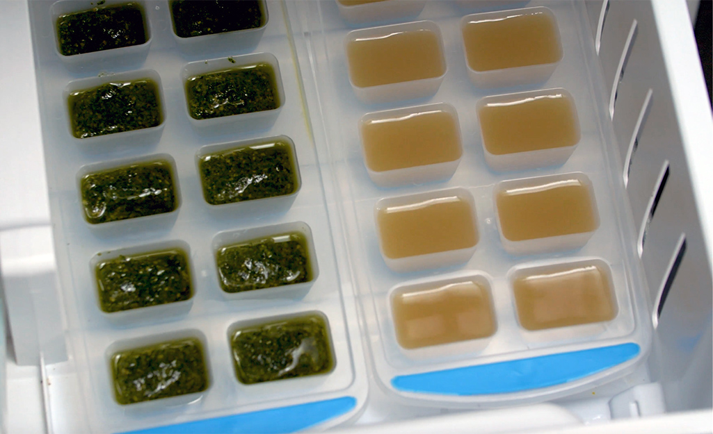 Pesto and soup stock in ice trays in a freezer. 