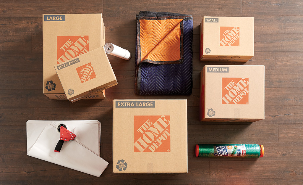 Home Depot boxes, moving blankets and packing paper lying on a wood floor.