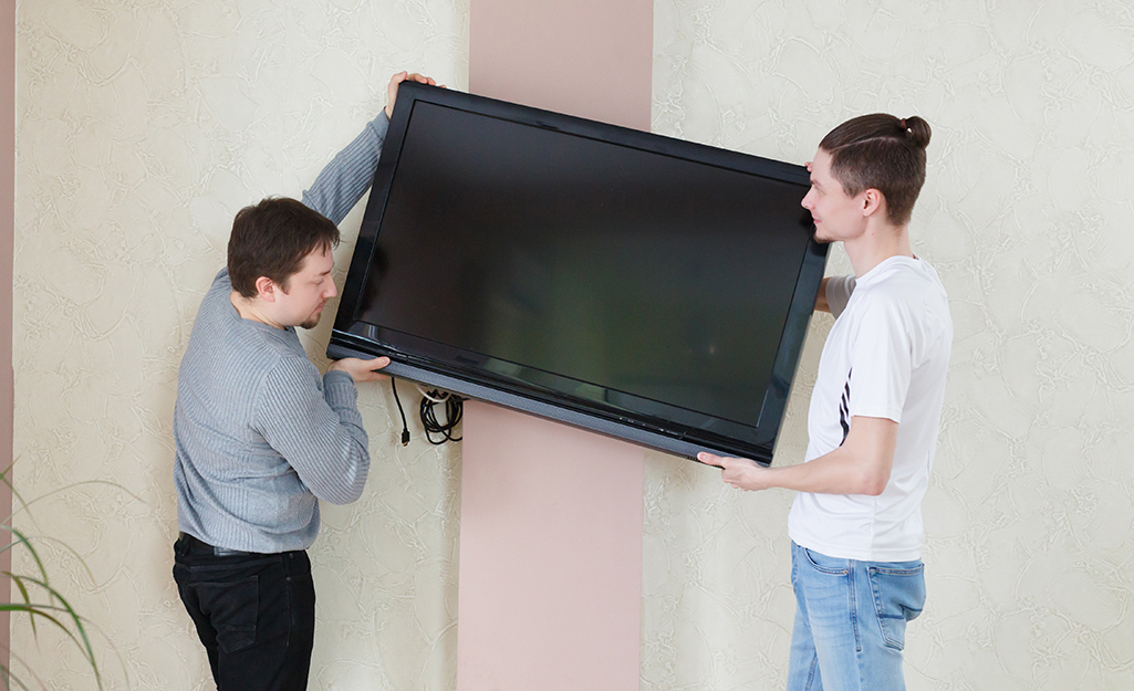 Two people mounting a flat screen TV to a wall.