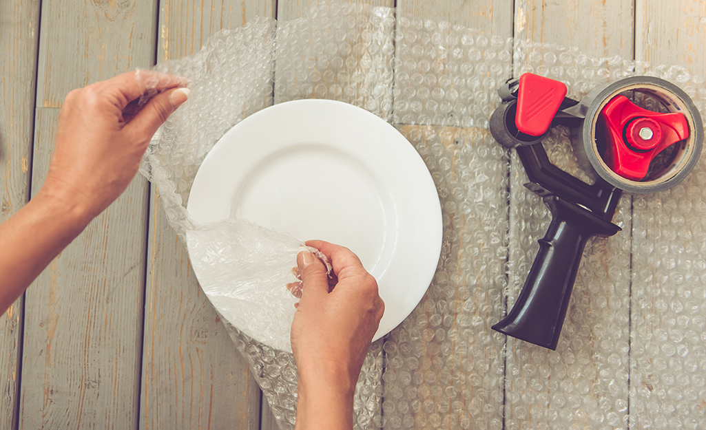 A person wrapping up a plate with bubble wrap and tape.