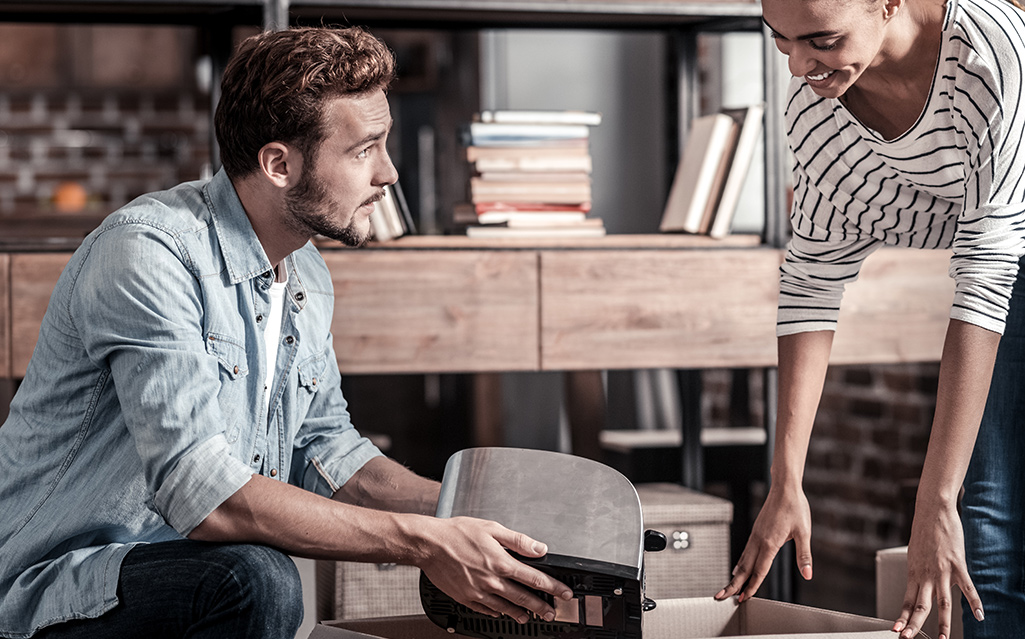 Two people placing a small appliance into a moving box.