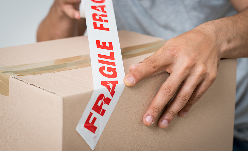 Man sticking tape that says fragile onto a moving box.