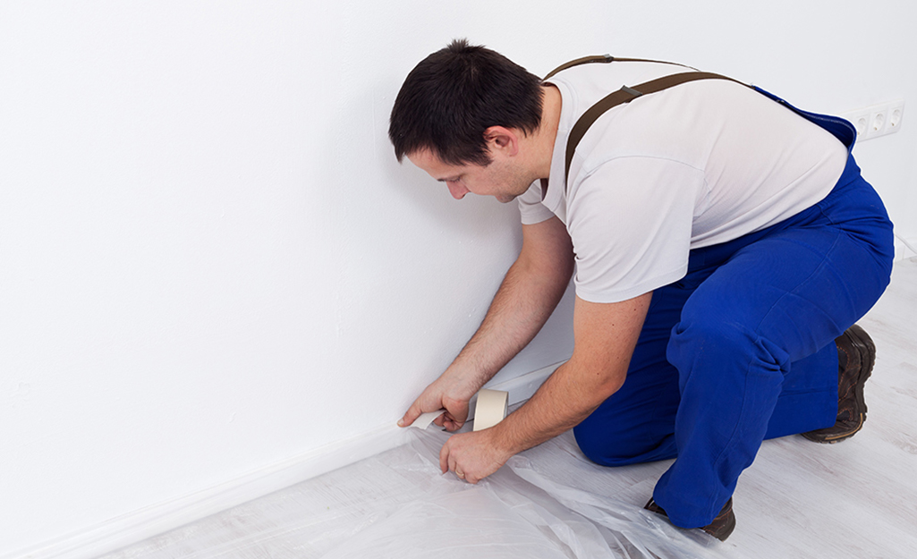 A man secures a drop cloth to a floor.