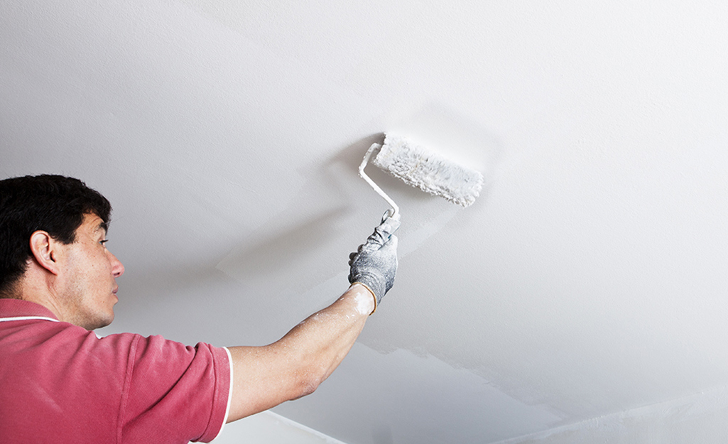 A man begins to paint the ceiling white using a roller.