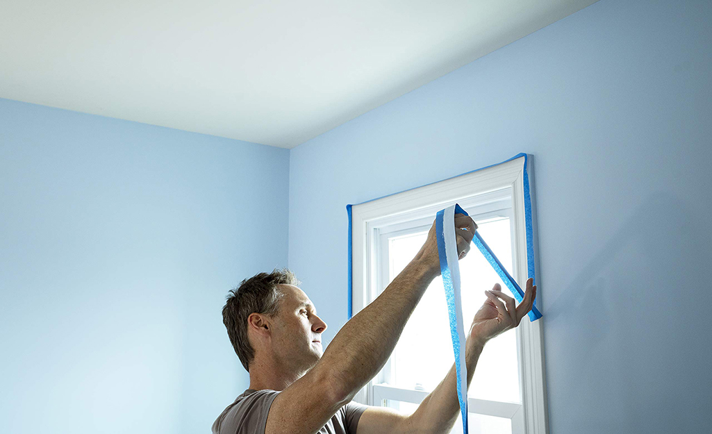 Man removing painter's tape from around a window.