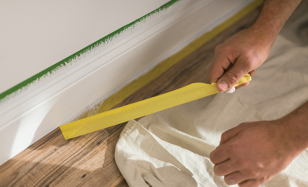 A person removing the tape from a baseboard.