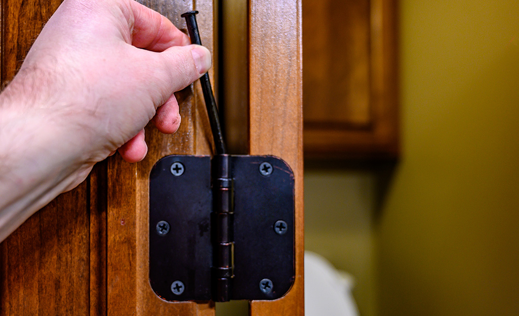 A person removing a pin from a door hinge.
