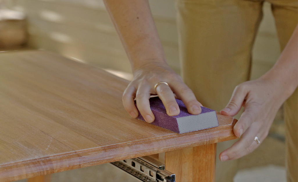 Someone sanding a small wood table before painting it.