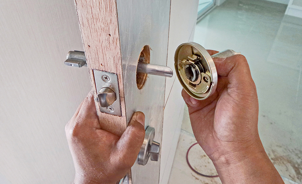 A person removes doorknob hardware from a door.