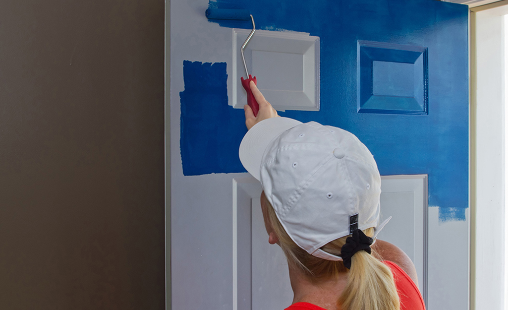 A person paints an attached interior door with a roller.